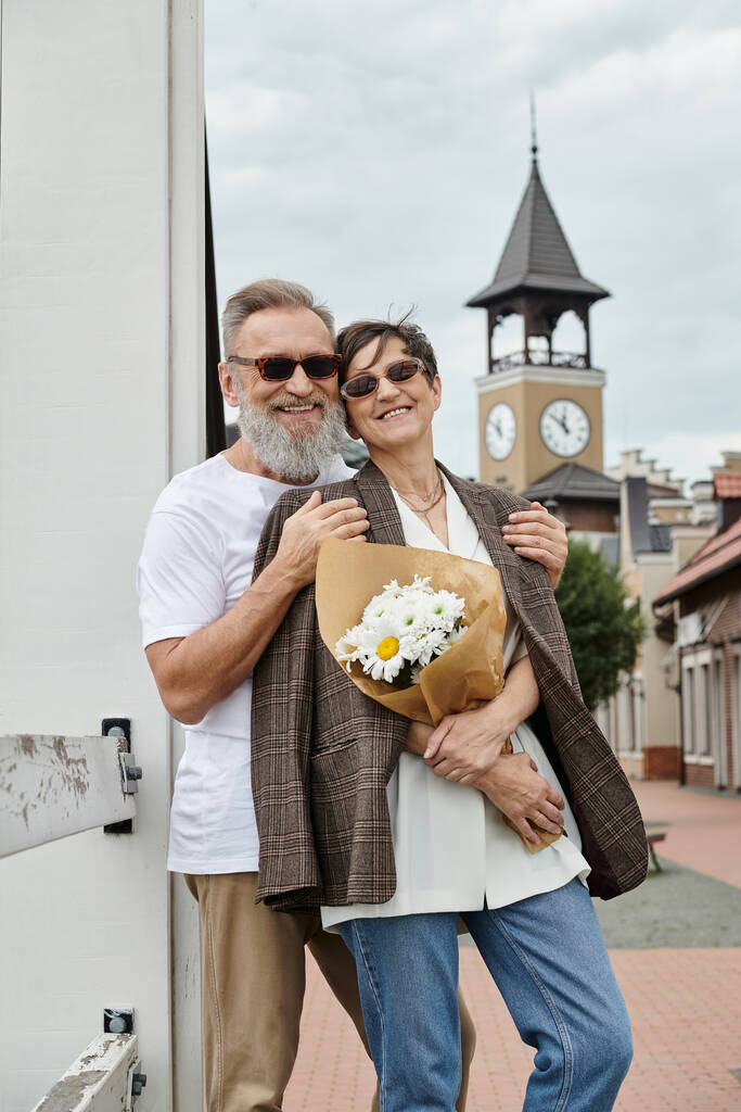 szczęśliwy starsi para w okularach przeciwsłonecznych, mężczyzna przytulanie kobieta z kwiatami, lato, outlet, bukiet, romans - Zdjęcie, obraz
