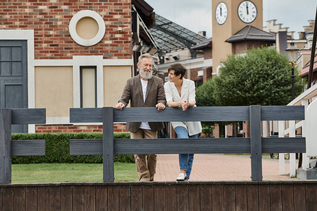 gelukkig ouder stel, vrouw kijkt naar man, staan in de buurt van hek, stedelijke achtergrond, vergrijzing van de bevolking - Foto, afbeelding