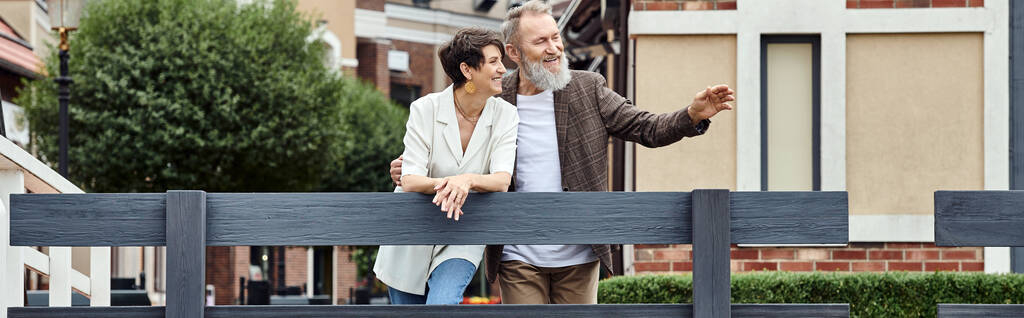 радостная пожилая пара, мужчина указывая на, единение, городской фон, старение населения, знамя - Фото, изображение