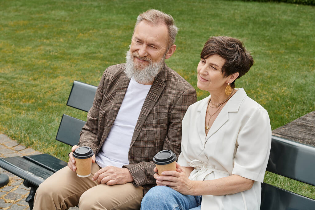 šťastný starší muž a žena sedí na lavičce, drží papírové kelímky s kávou, starší pár, romantika - Fotografie, Obrázek