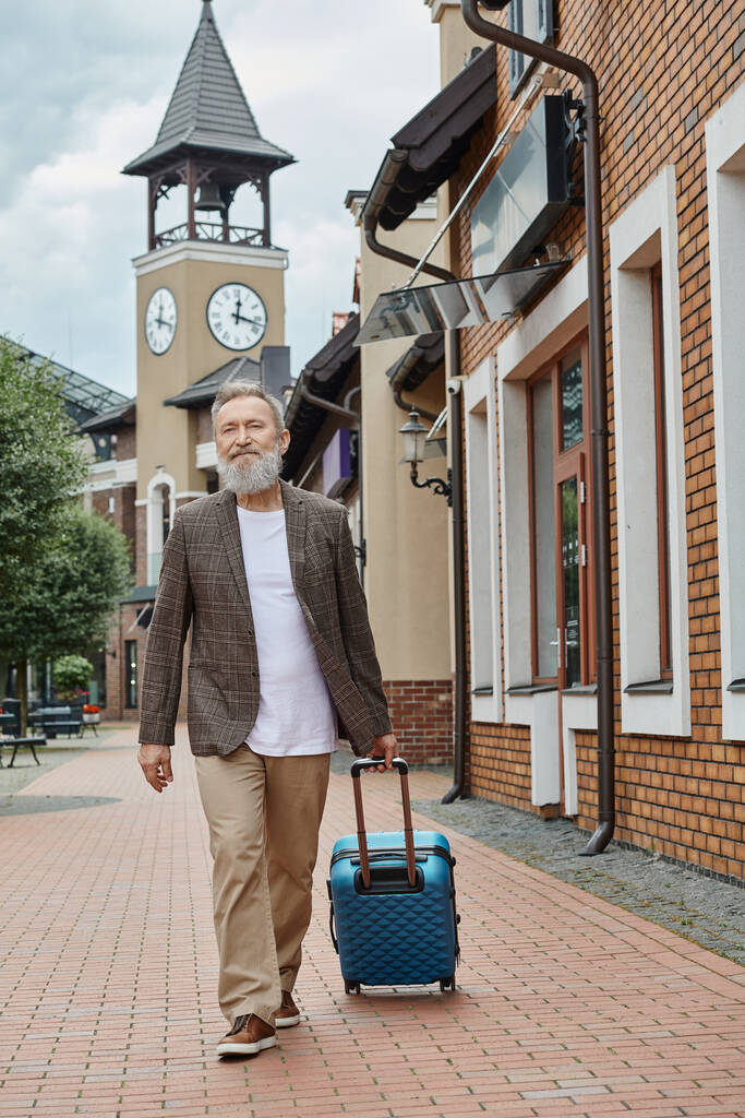 szakállas idős férfi séta poggyász a városi utcán, városi életmód, utazás, stílusos idős - Fotó, kép