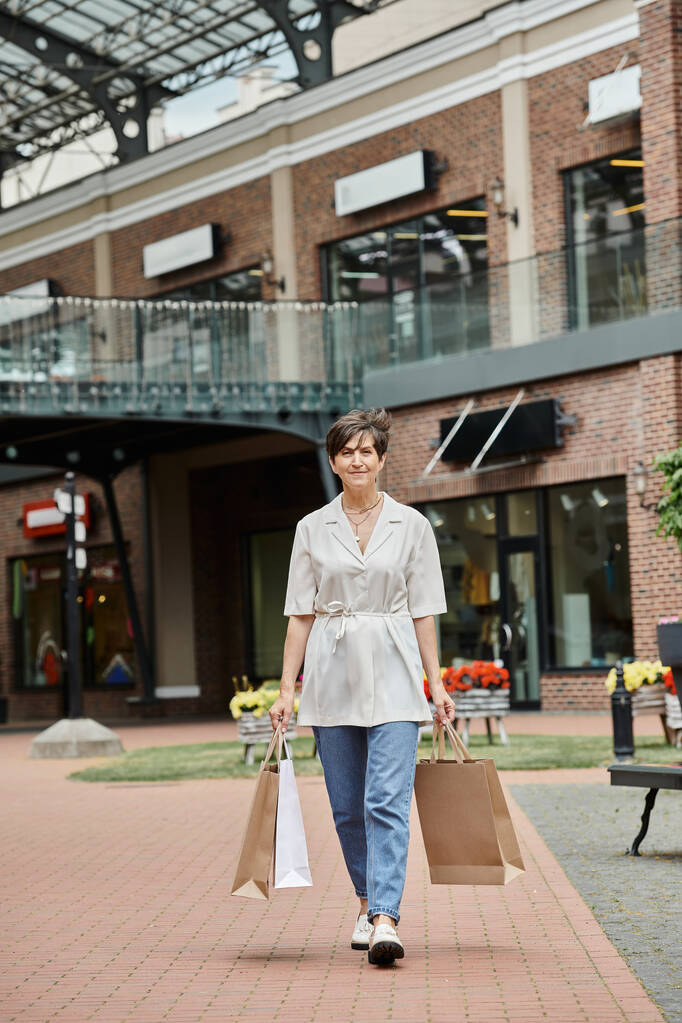 zadowolona seniorka spacerująca z torbami na ulicy miejskiej, handel detaliczny, starsze osoby w mieście, na zewnątrz - Zdjęcie, obraz