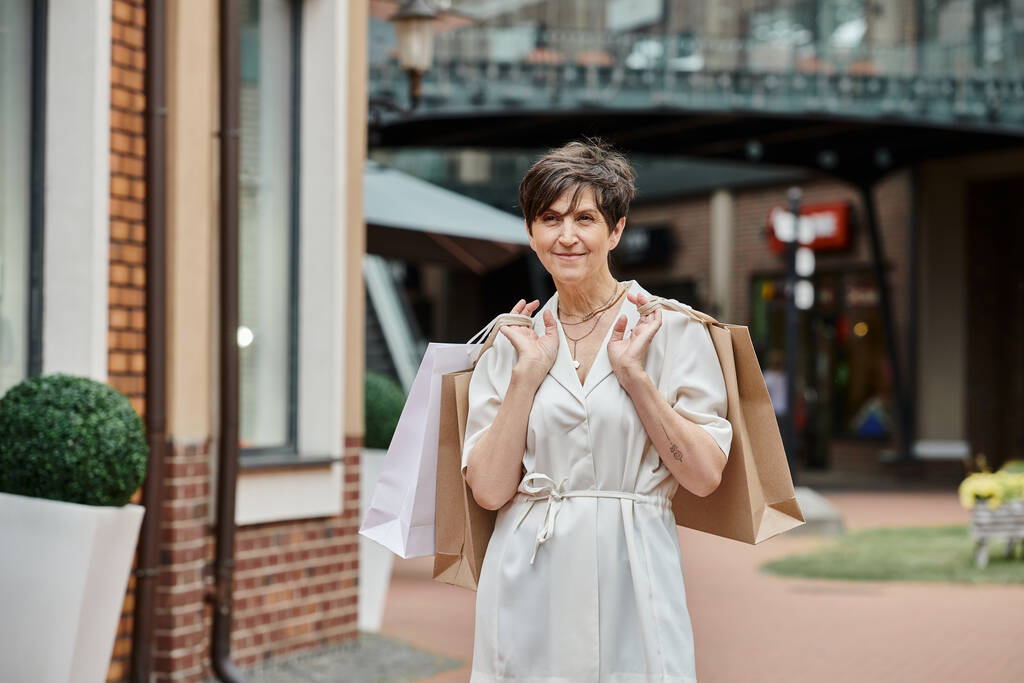 aging population, pleased senior woman holding shopping bags near outlet, active senior, positive - Photo, Image