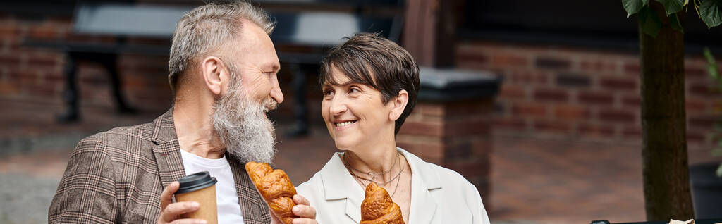 feliz pareja de ancianos sosteniendo croissants y café para llevar, taza de papel, al aire libre, pancarta horizontal - Foto, Imagen