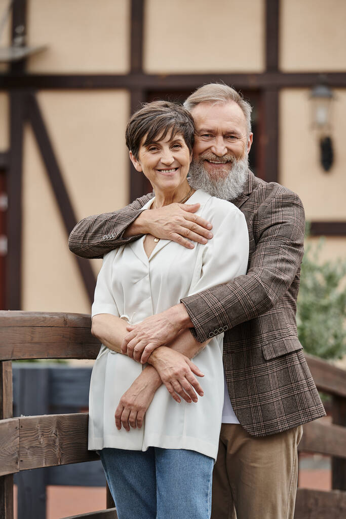 bearded man hugging woman, husband and wife, senior romance, happy, aging population, outdoors - Photo, Image