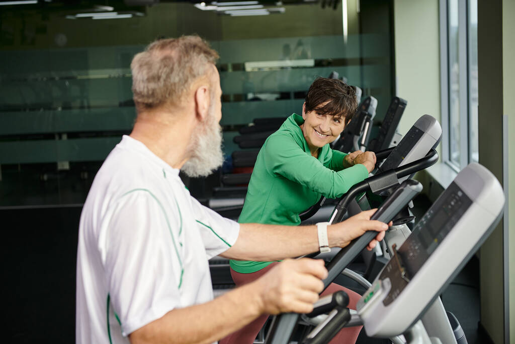 mujer alegre mirando al hombre de edad avanzada, marido y mujer haciendo ejercicio en el gimnasio, personas mayores activas, deporte - Foto, Imagen