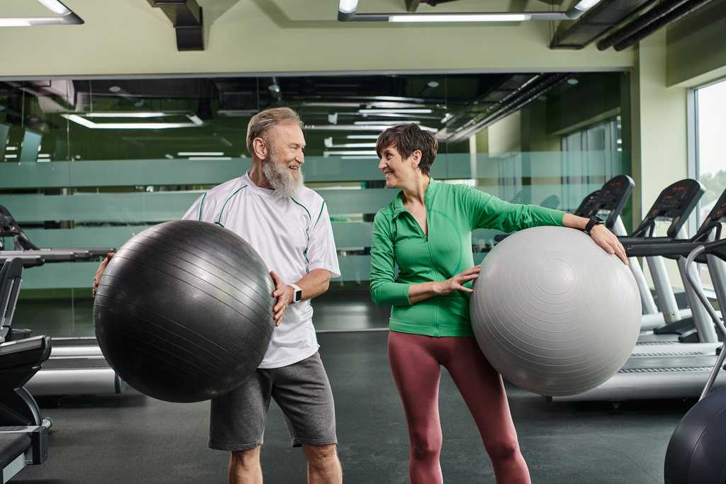 пожилая пара, счастливый мужчина и женщина держат фитнес-мячи, активные пожилые смотрят друг на друга - Фото, изображение