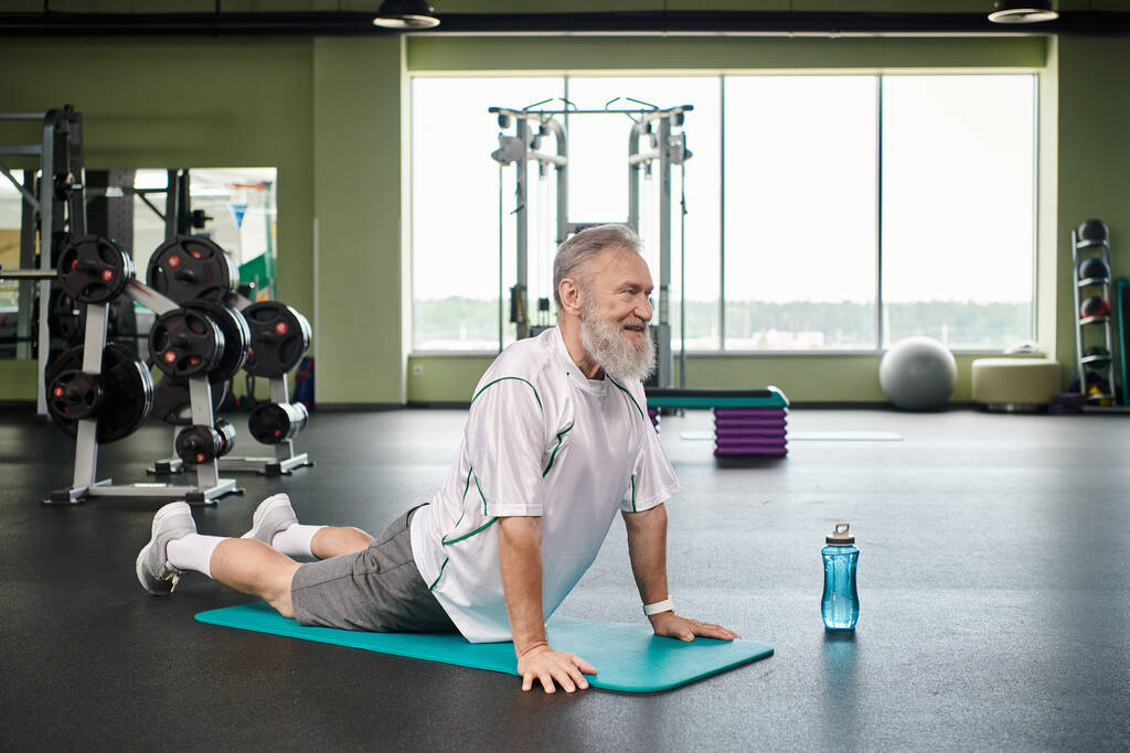 glücklicher älterer Mann mit zurückgestrecktem Bart auf Fitnessmatte, aktiver Senior, lebhaft und gesund - Foto, Bild
