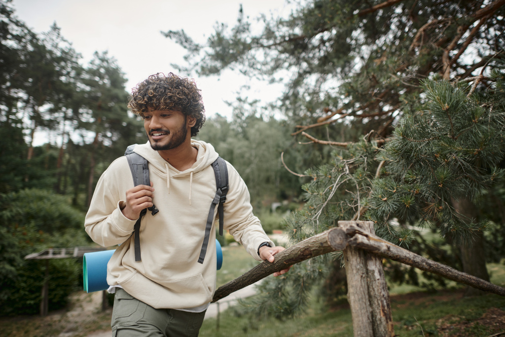 jovem caminhante índio sorridente com mochila andando perto de cerca na floresta turva - Foto, Imagem