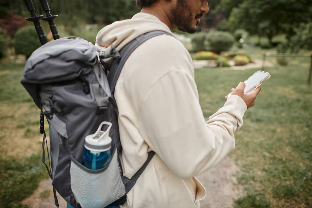 vista recortada de senderista indio con mochila usando teléfono inteligente en camino en el bosque - Foto, Imagen