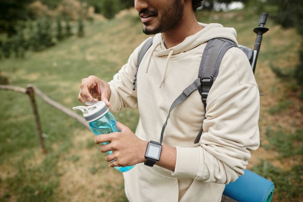 cropped view of indian tourist with backpack holding sports bottle outdoors - Photo, Image