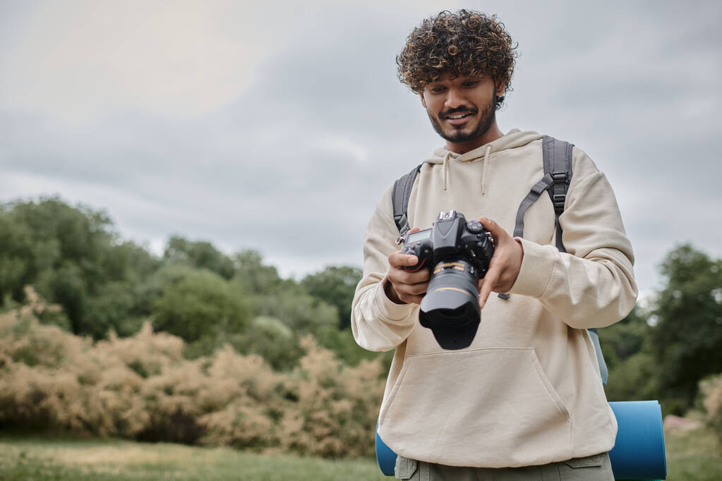 happy indian photographer in hoodie holding professional camera, travel and adventure concept - Photo, Image