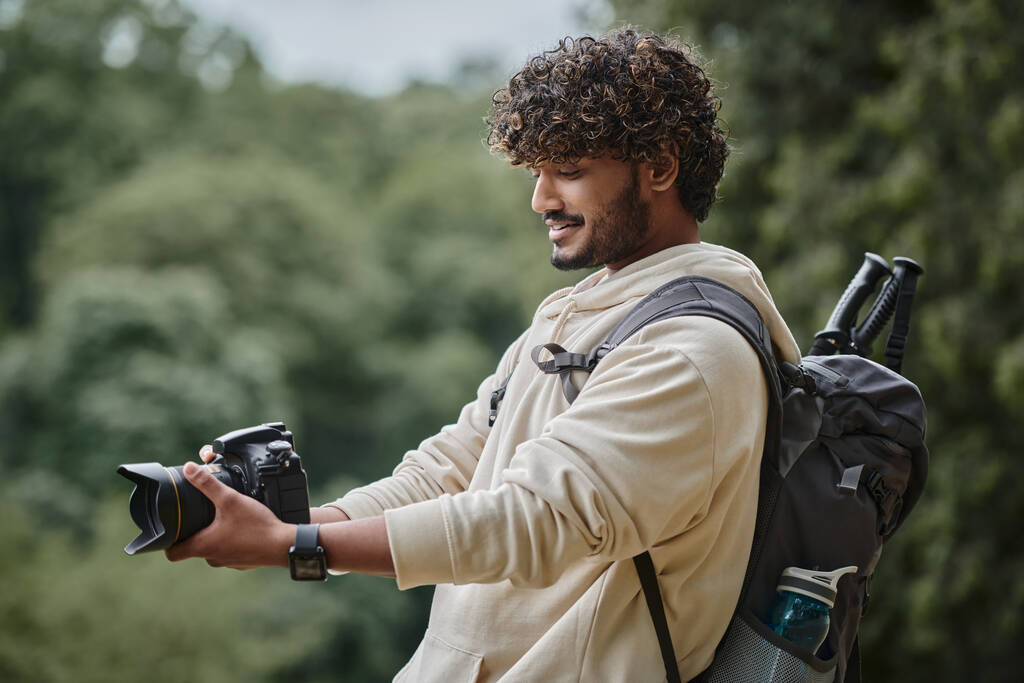 radosny indyjski turysta robiący zdjęcia na profesjonalnym aparacie fotograficznym, turysta z plecakiem w lesie - Zdjęcie, obraz