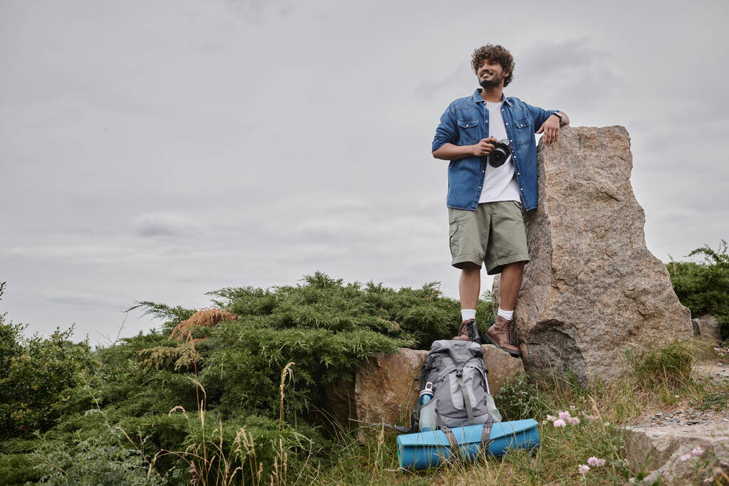 fotografía y concepto de la naturaleza, mochilero indio feliz sosteniendo cámara digital y de pie sobre roca - Foto, Imagen