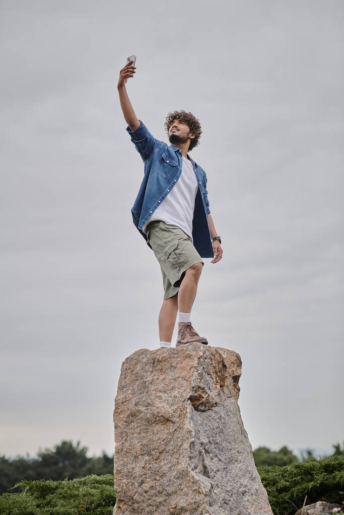nomadisme concept, bouclé homme indien debout sur le rocher et tenant smartphone, signal de recherche - Photo, image