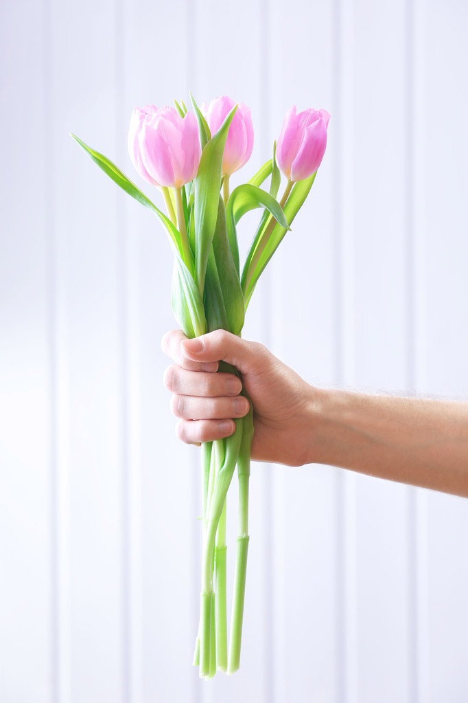 Mano sosteniendo hermosos tulipanes rosados sobre fondo de madera
 - Foto, imagen