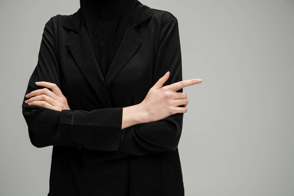 vista recortada de la mujer de negocios musulmana en chaqueta negra posando con los brazos cruzados en gris, confianza - Foto, Imagen