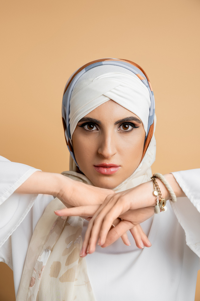 encantadora mujer de Oriente Medio en elegante bufanda de seda mirando a la cámara en beige, belleza musulmana - Foto, imagen