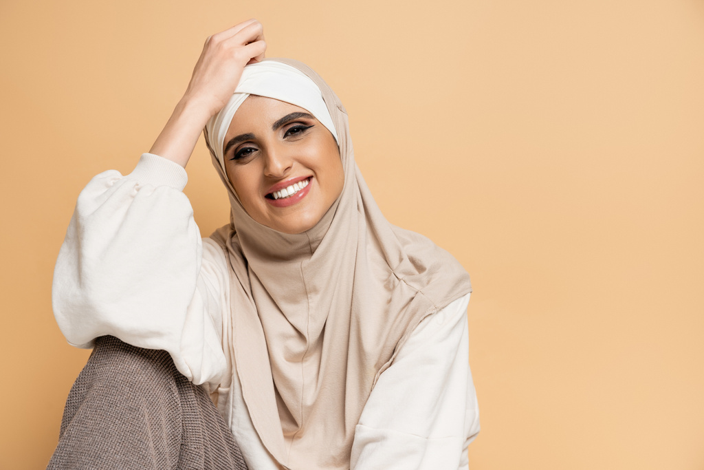 Makyajlı, tesettürlü ve modaya uygun giyinmiş bej renkli kameraya bakan çekici Müslüman kadın. - Fotoğraf, Görsel