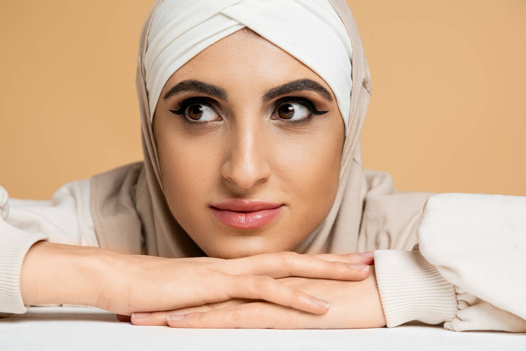 Nahaufnahme Porträt einer charmanten muslimischen Frau mit Make-up, die am Tisch sitzt und beige wegsieht - Foto, Bild