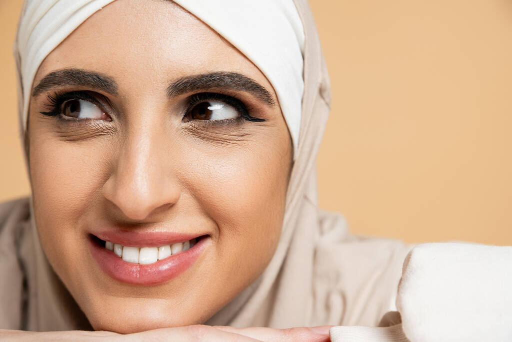 close up portrait of smiling muslim woman with makeup, in hijab, looking away on beige - Photo, Image
