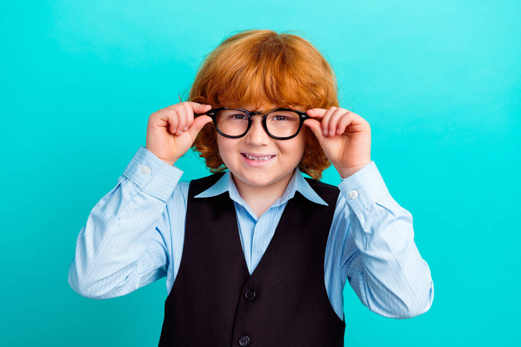 Foto von niedlichen intelligenten positiven Schulkind Arme berühren Brille strahlendes Lächeln isoliert auf teal Farbhintergrund. - Foto, Bild