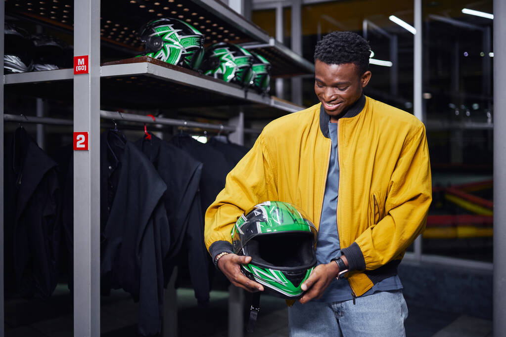 happy african american kart racer in yellow bomber jacket holding helmet, male driver, go-cart - Photo, Image