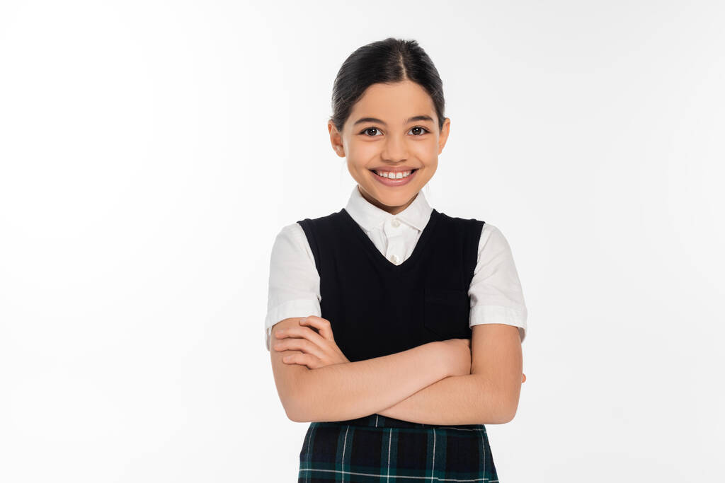 happy schoolgirl in black vest standing with folded arms and looking at camera isolated on white - Photo, Image