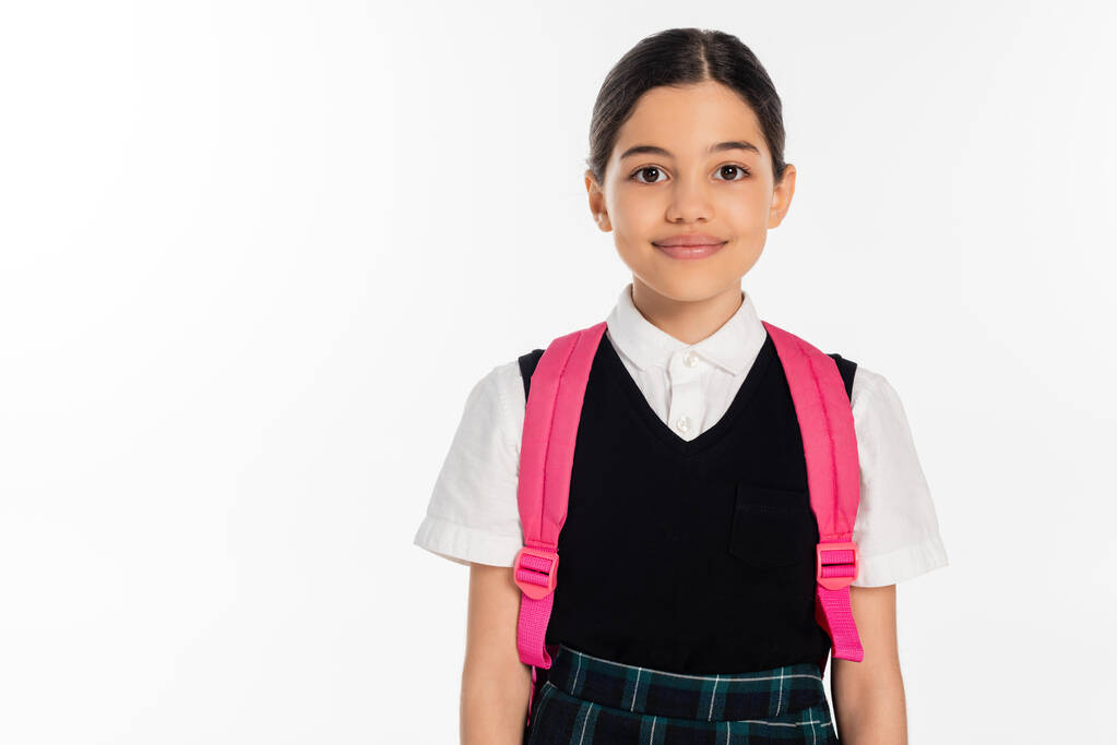 happy schoolgirl with pink backpack and black vest looking at camera isolated on white, student - Photo, Image