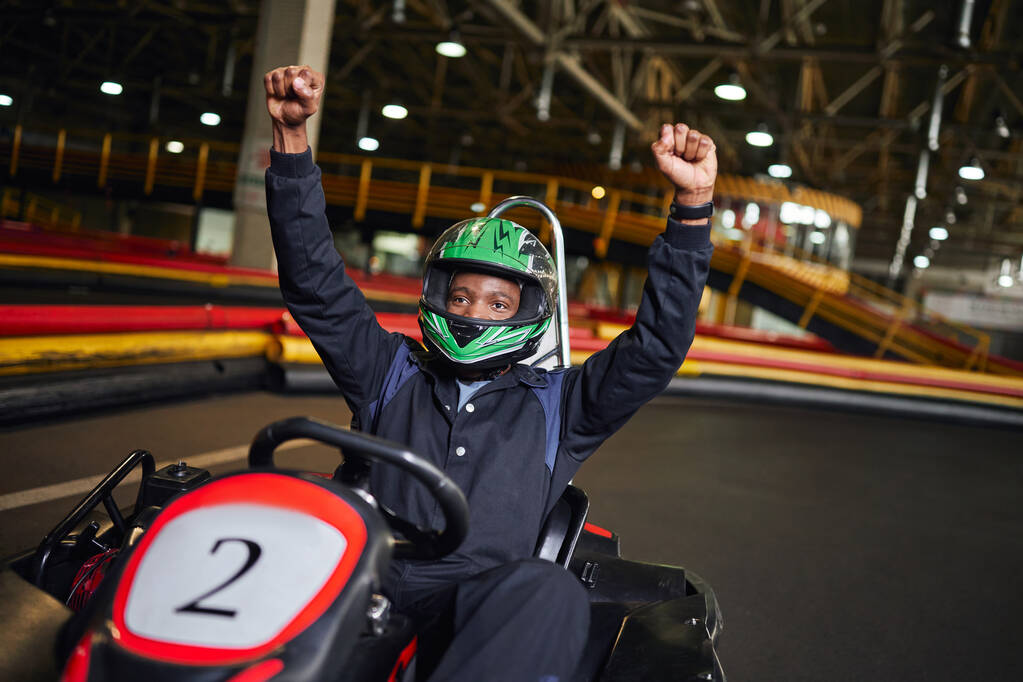 Go kart speed drive, excited african american driver in helmet raising hands and winning race - Photo, Image
