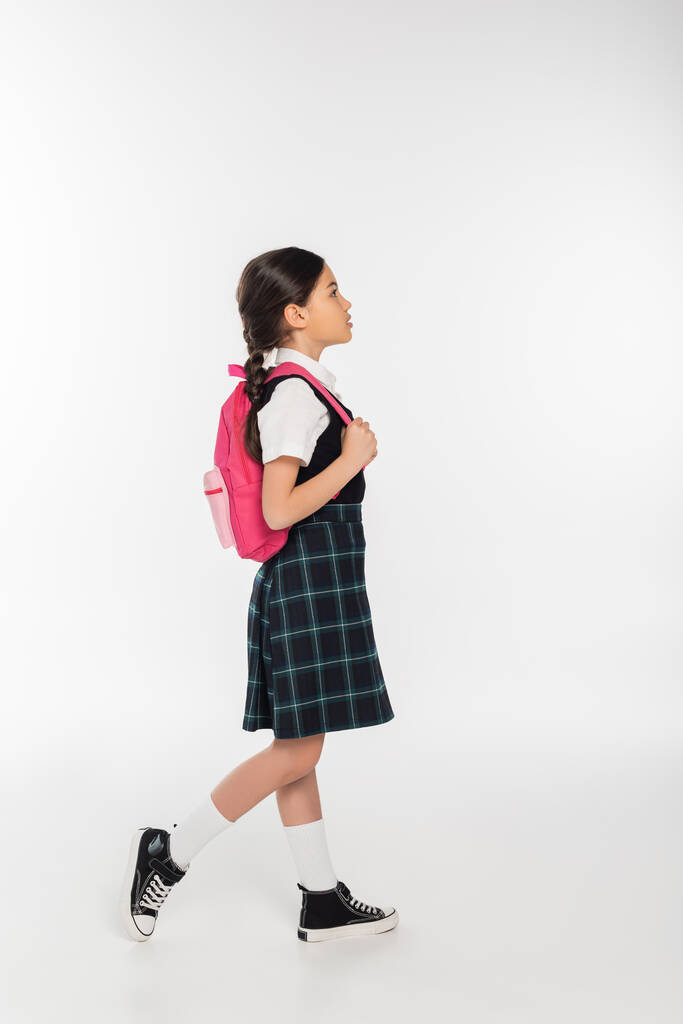 в полный рост, школьница в форме, стоящая с рюкзаком и отводящая взгляд, белый фон - Фото, изображение
