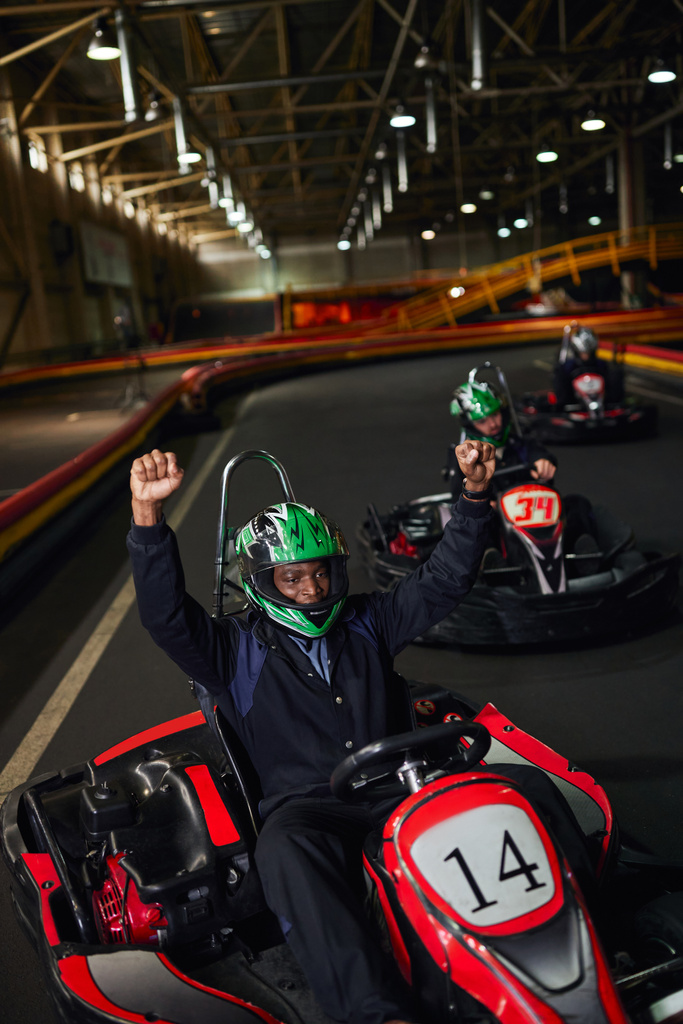 emocionado afroamericano ir conductor de carro en el casco levantando las manos y ganar la carrera en circuito, go-kart - Foto, Imagen