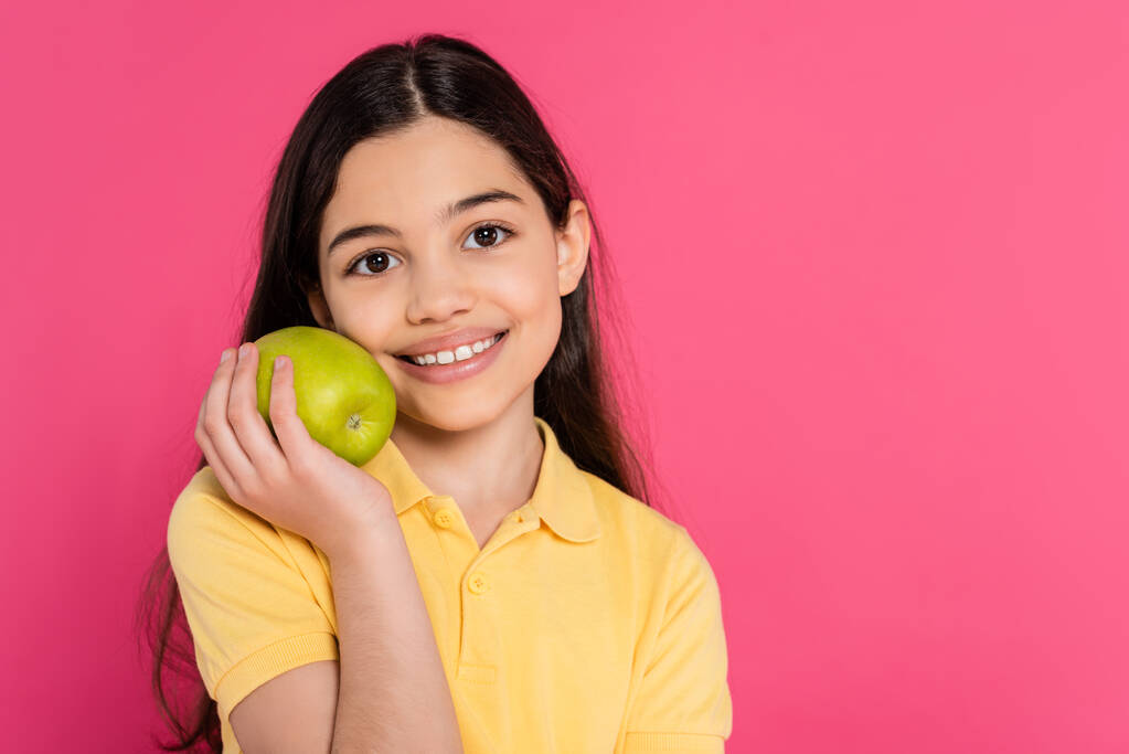 portrait of happy brunette girl holding green and fresh apple isolated on pink, vibrant backdrop - Photo, Image