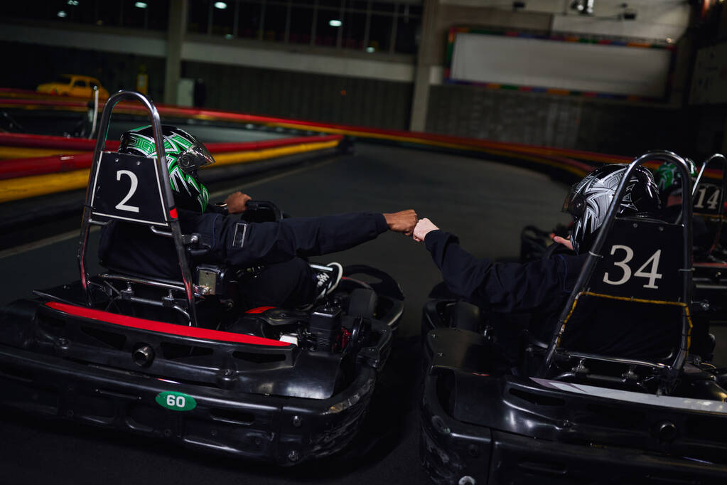 dois go kart motoristas em sportswear e capacetes punho batendo e sentado em carros esportivos para karting - Foto, Imagem