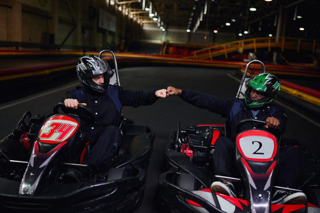 Diverse Go-Kart-Fahrer mit Helmen schlagen die Faust und sitzen in Sportwagen zum Kartfahren auf der Rennstrecke - Foto, Bild