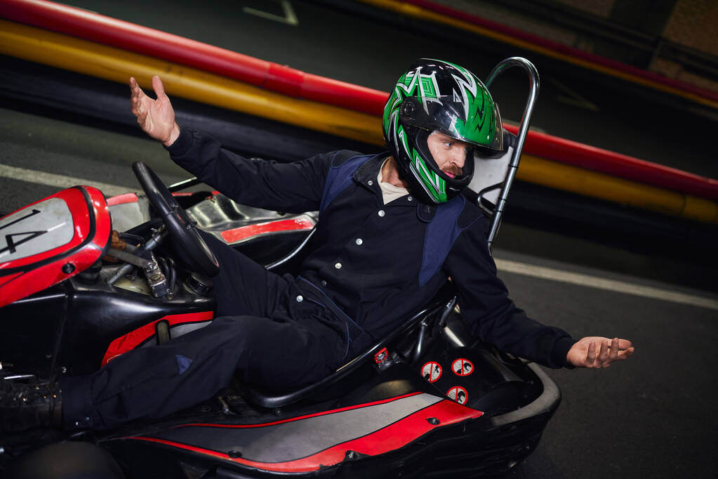 эмоциональный водитель в шлеме жестом во время вождения спортивного автомобиля для картинга на внутреннем кольце - Фото, изображение