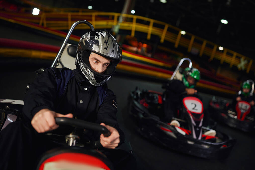 geconcentreerde diverse mannen in helmen rijden go kart op indoor circuit, autosport en adrenaline - Foto, afbeelding