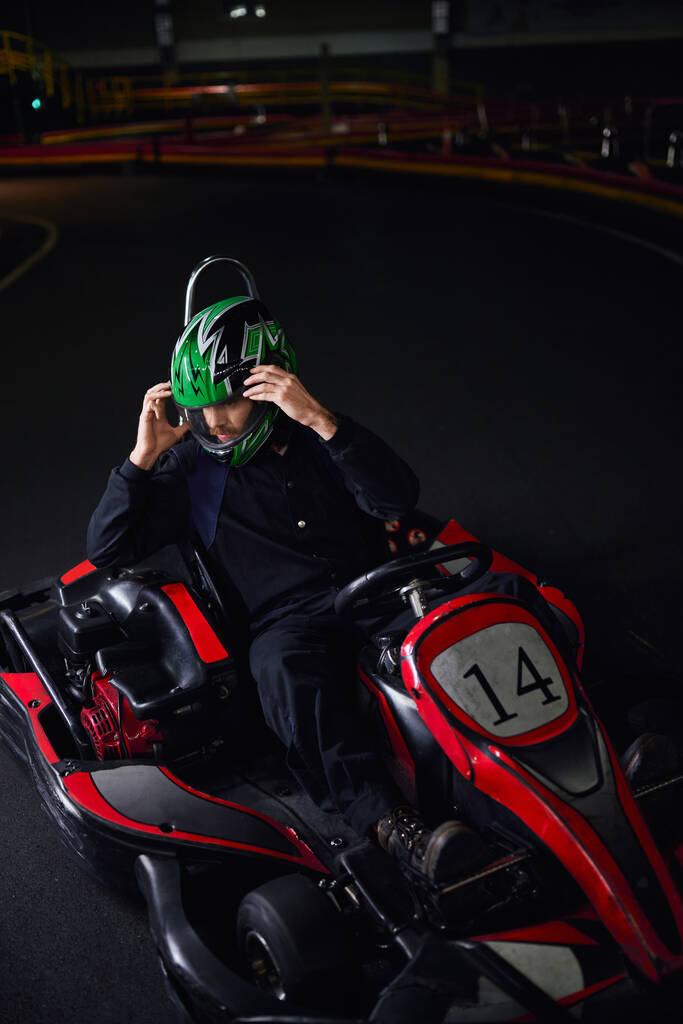 uomo che si toglie il casco e si siede in go kart dopo gara sul circuito indoor, concetto adrenalina - Foto, immagini