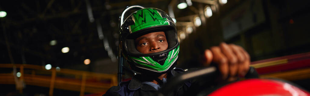 Afrikaans-Amerikaanse go cart racer in helm rijden op indoor circuit, speed racing uitdaging, banner - Foto, afbeelding
