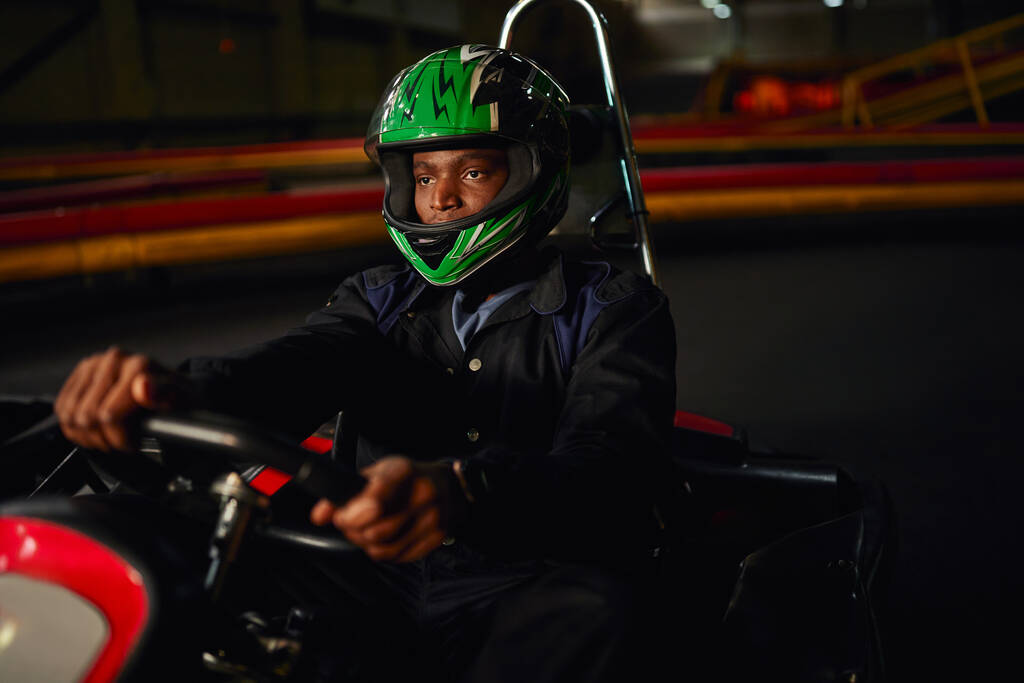 Afrykański amerykański go kart kierowcy w kasku jazdy na torze wewnątrz, prędkość wyścigów wyzwanie - Zdjęcie, obraz