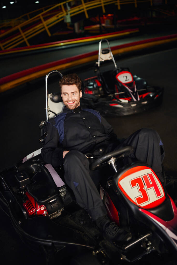屋内サーキットの中のレーシングカーに座っているスポーツウェアの陽気なゴーカートドライバー,勝者 - 写真・画像
