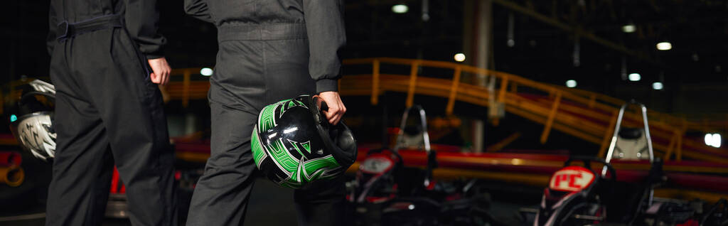 スポーツウェアのゴーカートドライバーがサーキットを歩き,ヘルメット,バナーを保持する様子 - 写真・画像