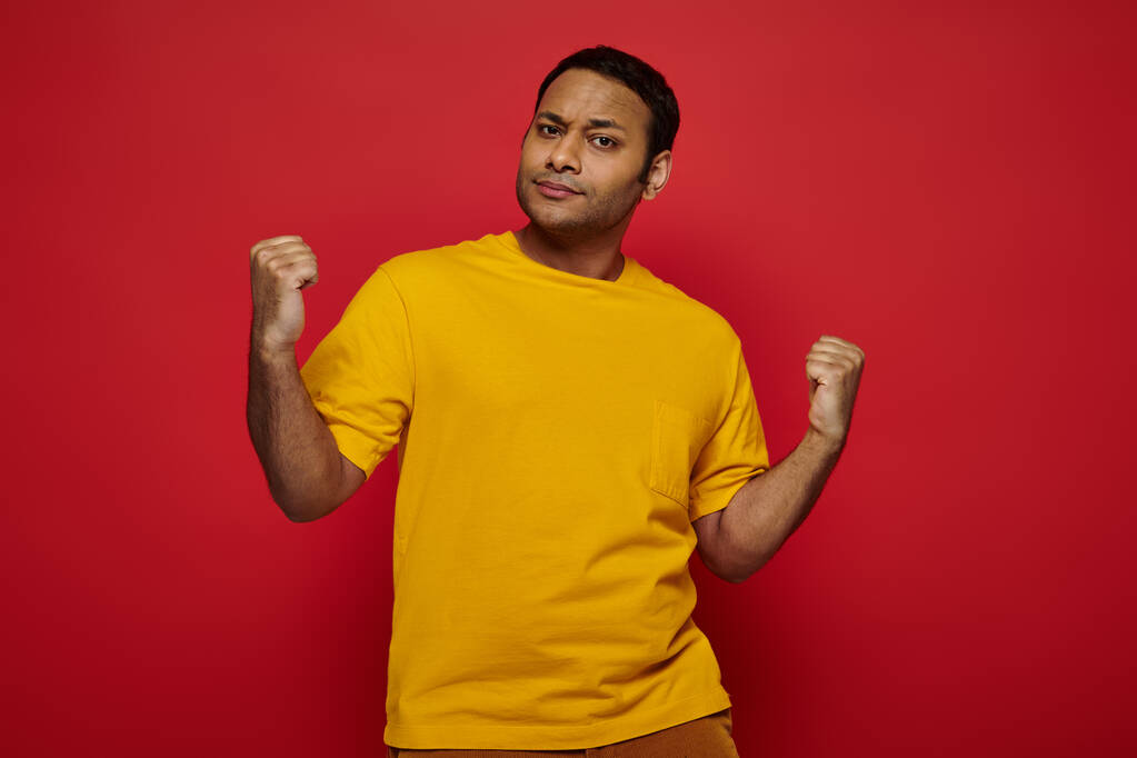 expressive indian man in casual clothes standing with clenched fists  on red background, strength - Photo, Image