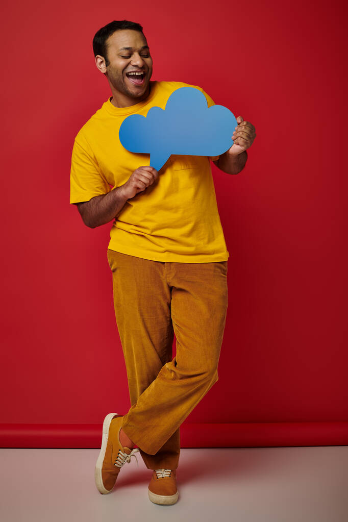 šťastný muž ve žlutém tričku drží prázdnou myšlenkovou bublinu na červeném pozadí, veselý obličej - Fotografie, Obrázek