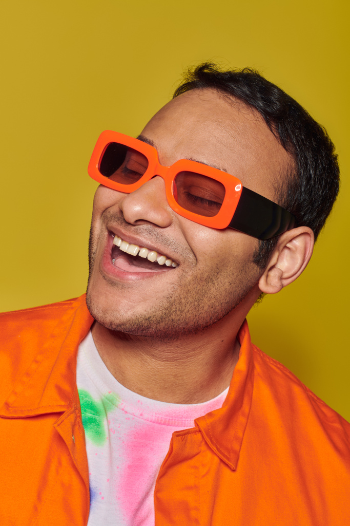 Kendini ifade etme kavramı, parlak turuncu güneş gözlüklü mutlu Hintli adam sarı arka planda gülümsüyor. - Fotoğraf, Görsel