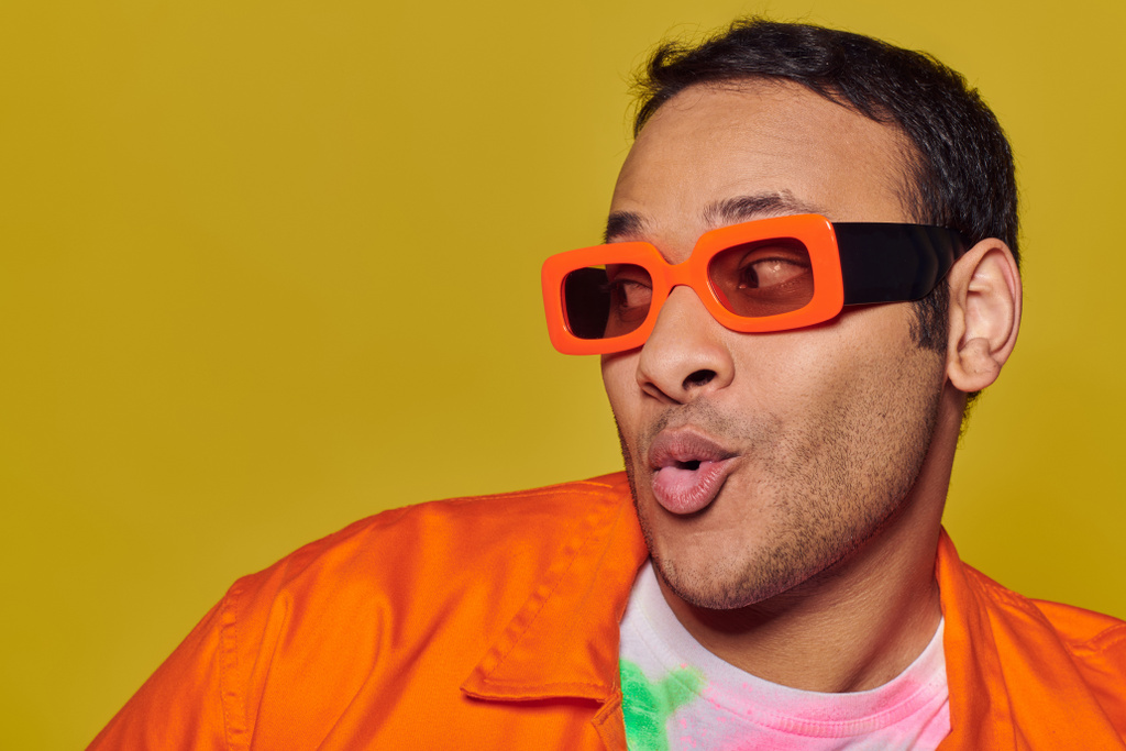 concept d'expression personnelle, homme indien surpris en lunettes de soleil orange regardant loin sur fond jaune - Photo, image