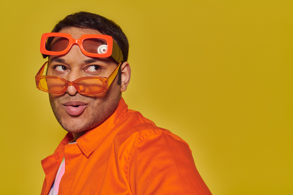 modny Indianin człowiek przymierza różne modne okulary przeciwsłoneczne i odwracając wzrok na żółtym tle - Zdjęcie, obraz