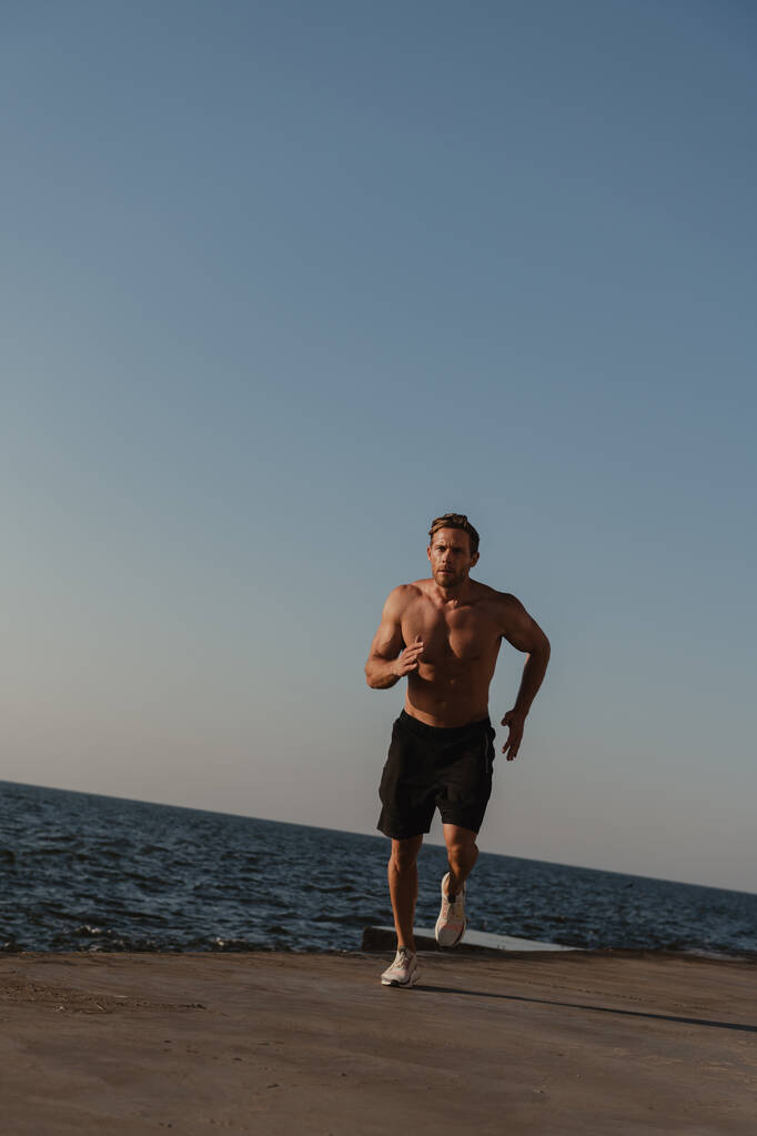Hombre atlético seguro corriendo al aire libre con el mar en el fondo - Foto, imagen
