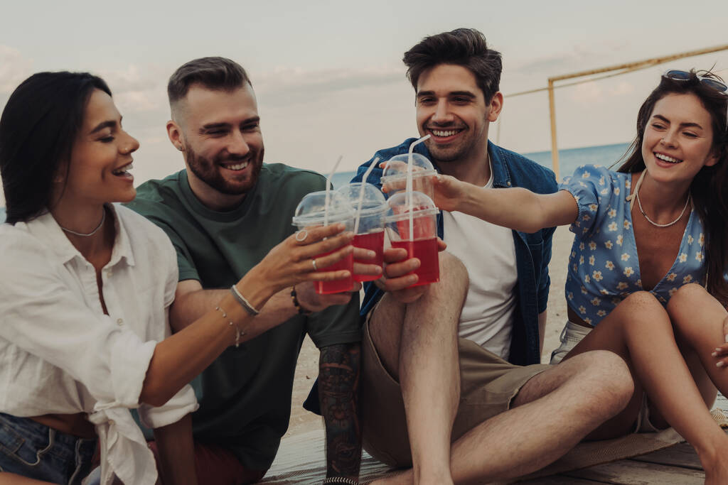 Група веселих молодих людей готує з коктейлями, проводячи час на пляжі разом - Фото, зображення