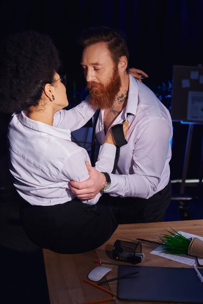 szakállas tetovált férfi elcsábítja afro-amerikai nő közel rendetlenség munkahelyi asztal az irodában, szerelem viszony - Fotó, kép